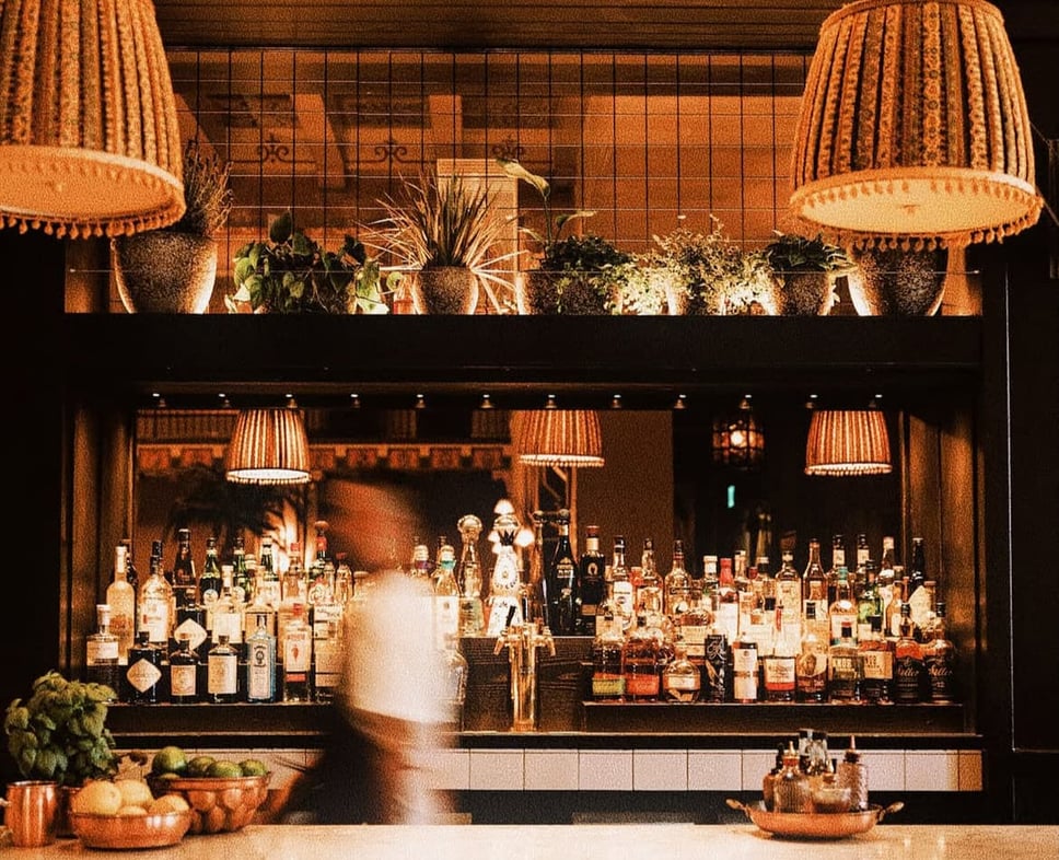 The bar at Gable inside The Hollywood Roosevelt, backed by pleated lamps and shelves of spirits