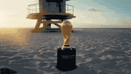 The FIFA World Cup trophy sits on a sandy beach with a lifeguard tower in the background.