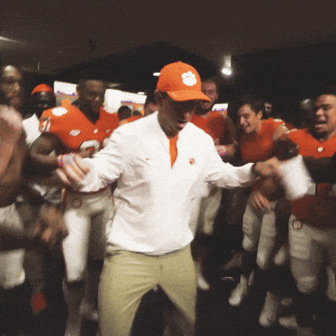 Clemson football coach Dabo Swinney dances in a locker room while players celebrate around him.