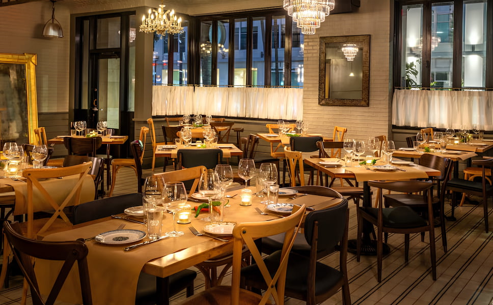 Malka dining room with wooden tables, upholstered chairs, chandeliers, and tall windows.