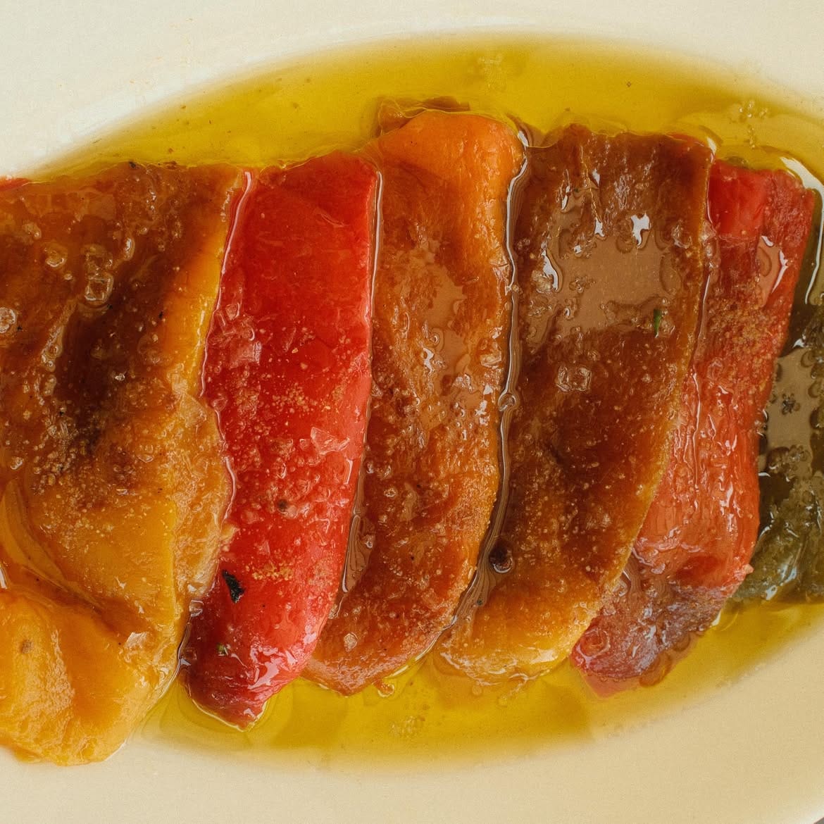 Roasted red and golden pepper strips in oil on a white plate.