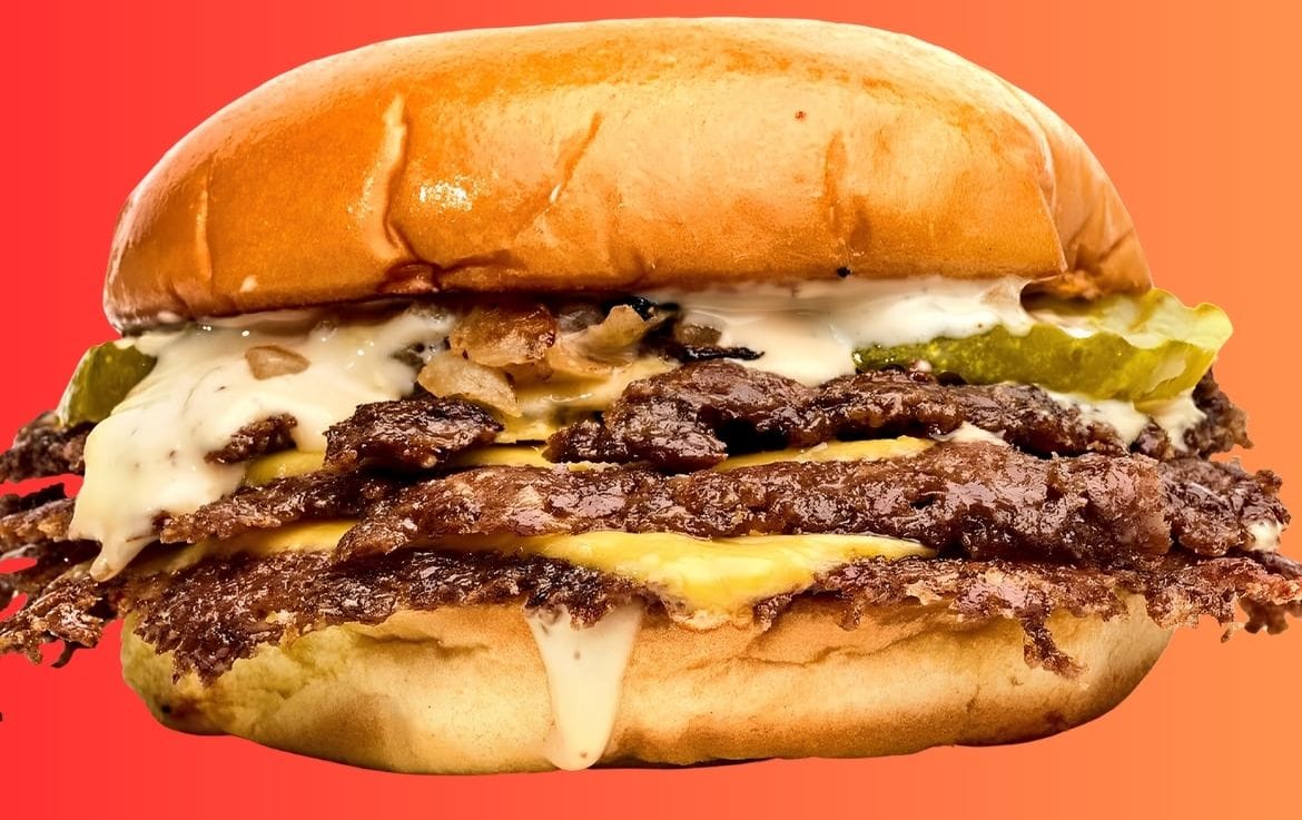 A 10/10 Burger smashburger with melted cheese, pickles and sauce against an orange background.