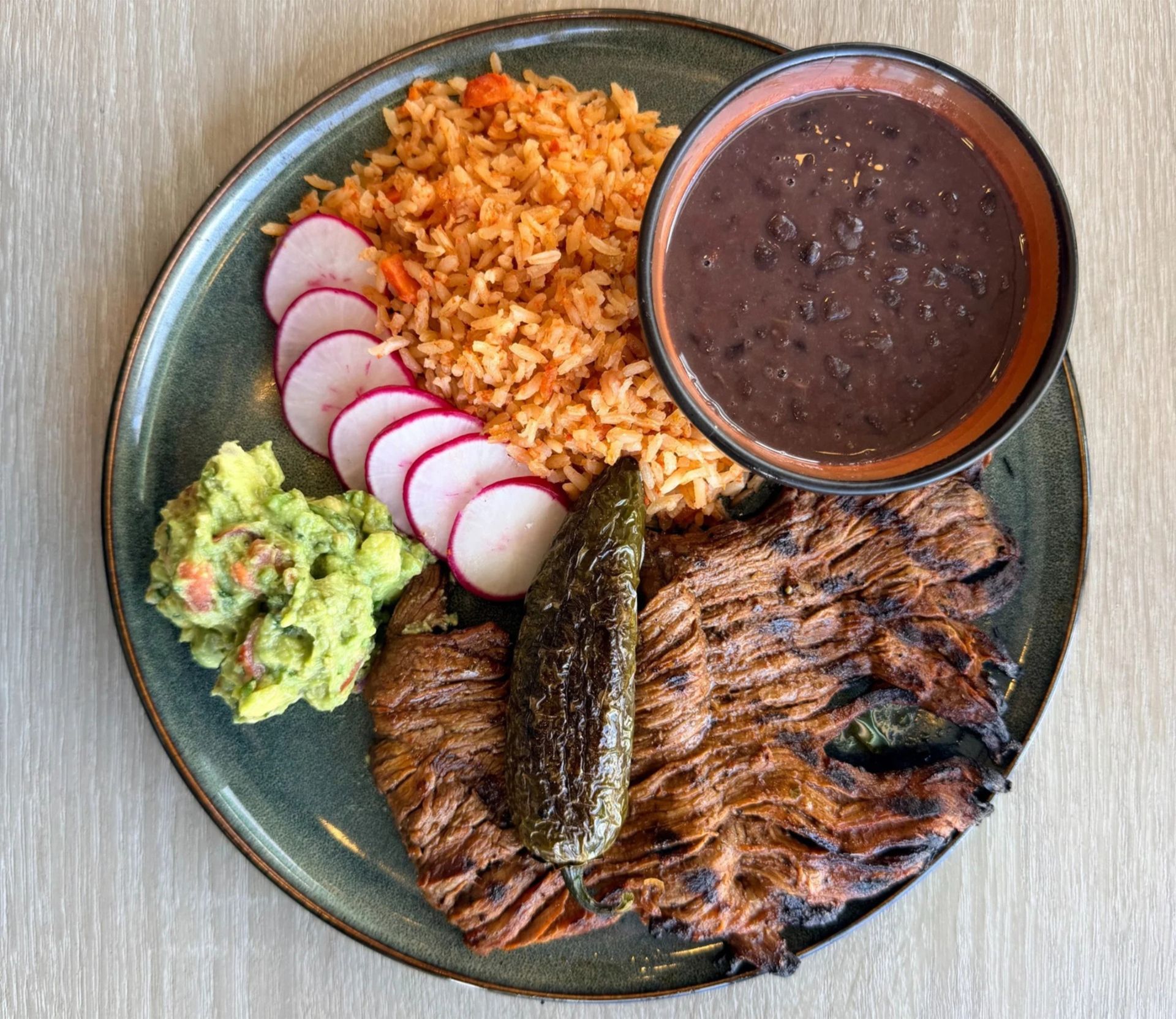 Cocina Victorias plate with grilled carne, rice, beans, guacamole and radishes.