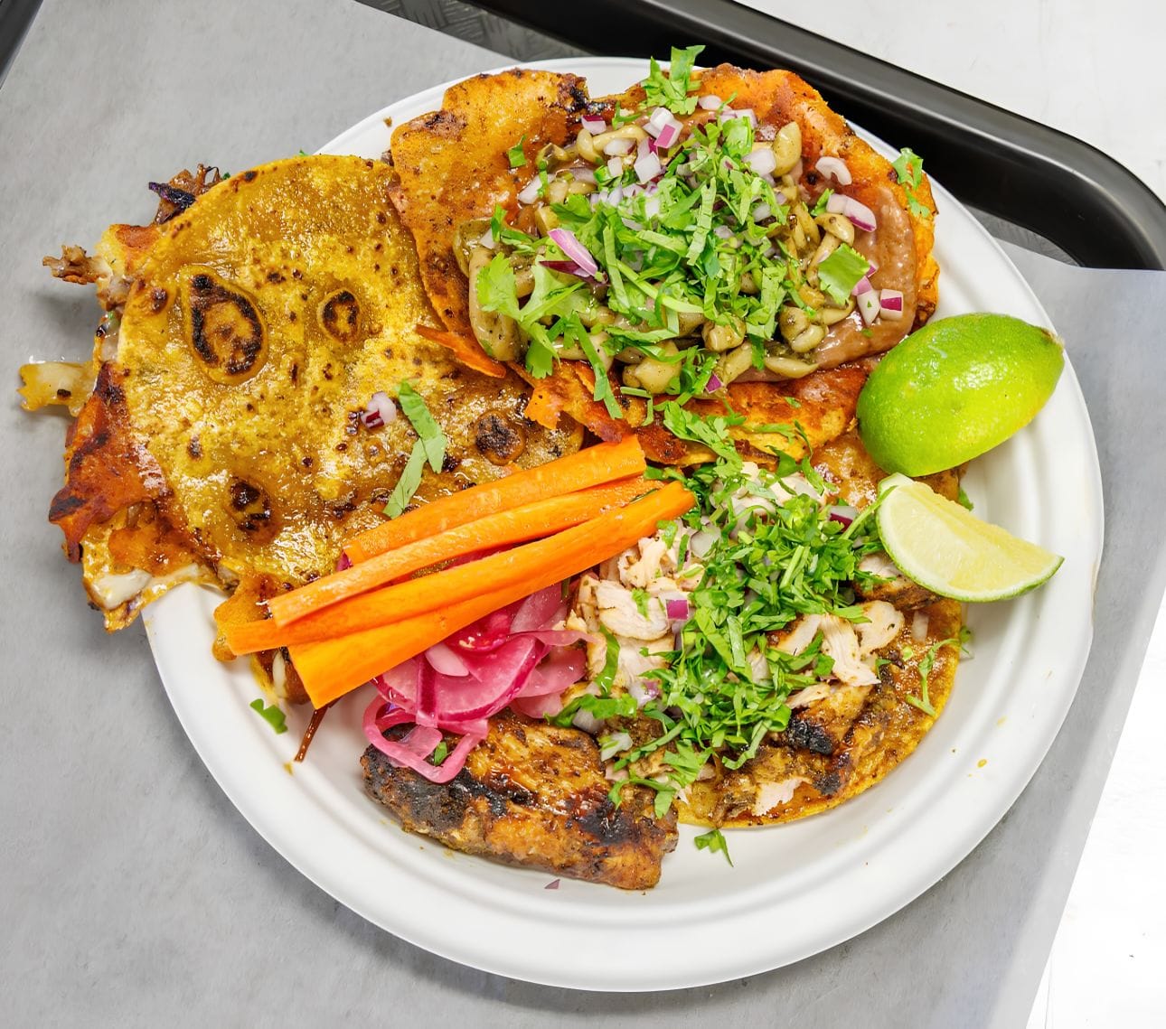 Birria Pa La Cruda tacos topped with cilantro and onion, served with lime and pickled vegetables.