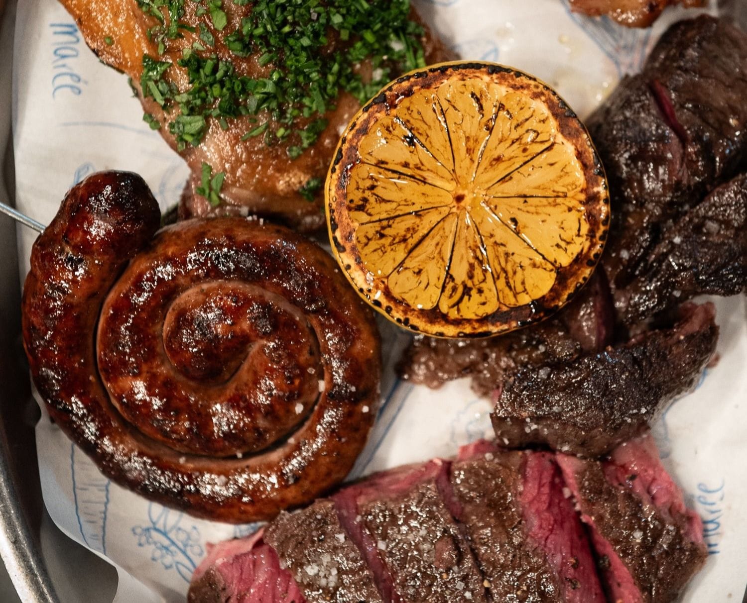 Marée dishes including sliced steak, sausage, and grilled lemon.